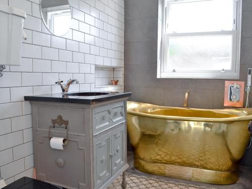 baño con bañera de oro y lavamanos en Coastguard Cottage, en Chestfield