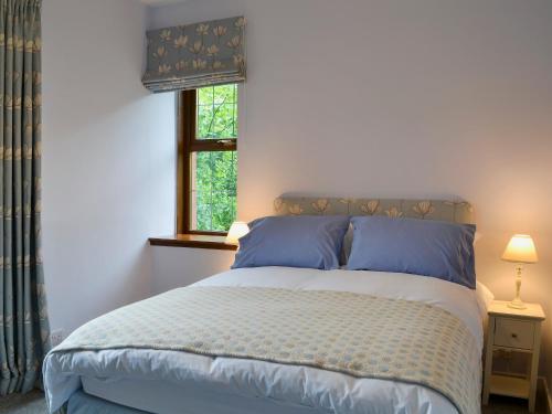 a bedroom with a bed with blue pillows and a window at Perch Hall Cottage in Dinwoodie Mains