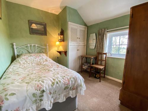 FrostendenにあるApril Cottageの緑の壁のベッドルーム1室、花柄のベッドカバー付きのベッド1台が備わります。