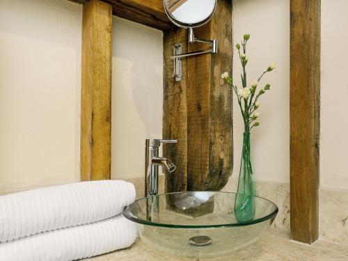 uma casa de banho com um lavatório de vidro e um vaso com flores em Chilsham Barn em Herstmonceux