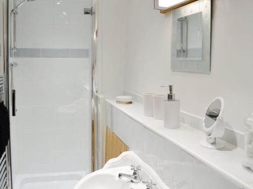 a white bathroom with a sink and a shower at Mill Meadow Cottage in East Down