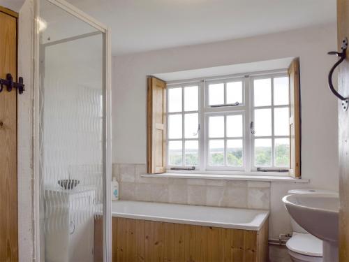 baño con bañera, lavabo y ventana en South View Cottage, en Chadlington