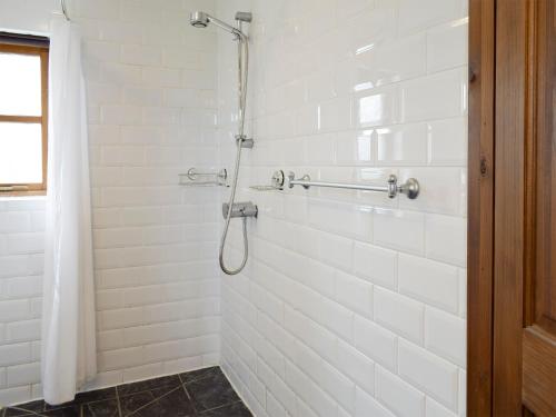 a white tiled shower with a shower curtain in a bathroom at Bryncrwn Cottage in Rhyd-y-felin