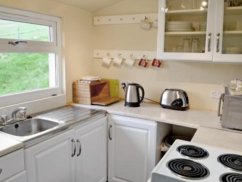 uma cozinha com armários brancos, um lavatório e um fogão em Glentairre Cottage - Swww em Balnaboth