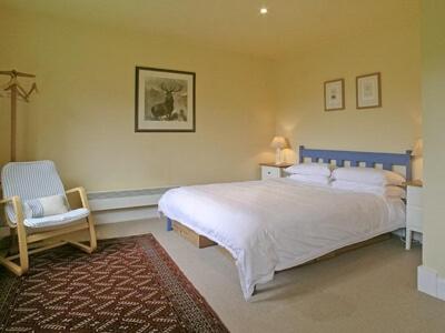 a bedroom with a large white bed and a chair at Ardura Cottage in Lochdon