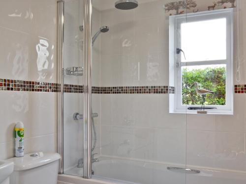 a bathroom with a shower and a toilet and a window at Stable Cottage in Lyminster