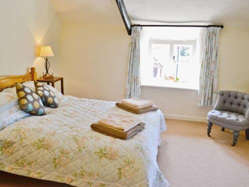 a bedroom with a bed and a chair and a window at Folly Cottage in Kentisbeare