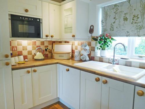 a kitchen with white cabinets and a sink and a window at Wold View Cottage in Rillington
