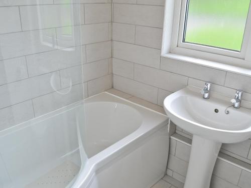 a white bathroom with a sink and a tub and a toilet at Eider Cottage in Embleton