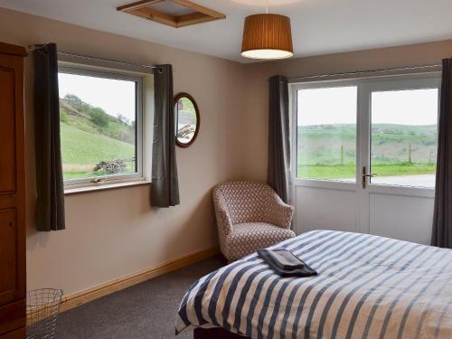 a bedroom with a bed and a chair and two windows at Booth Farm Cottage in Buxton