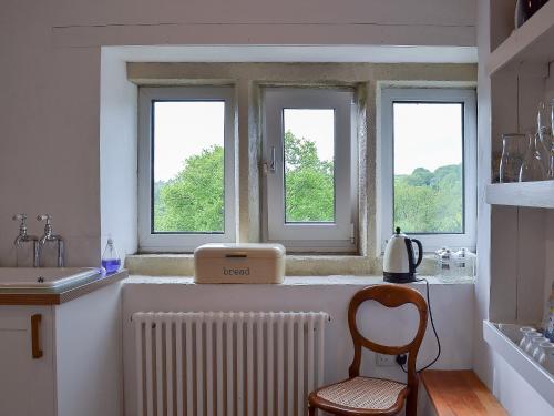 a kitchen with three windows and a radiator and a chair at Pear Tree House Annexe in Holmfirth