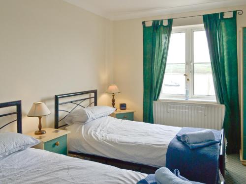 a bedroom with two beds with green curtains and a window at Tamar View in Saltash