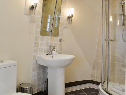 uma casa de banho com um lavatório branco e um chuveiro em The Windmill em Coedana