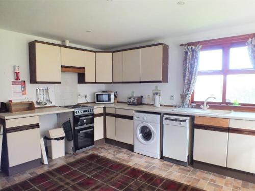 a kitchen with white cabinets and a washer and dryer at Olafs Cottage in Garlieston