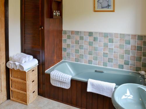 a bathroom with a bath tub and a sink at Half Moon Cottage in Martham