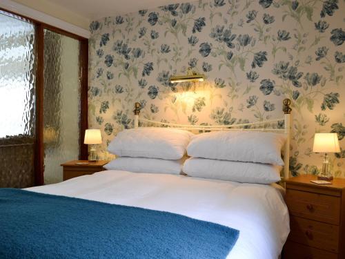 um quarto com uma cama branca e papel de parede floral em The Coach House em Drybrook