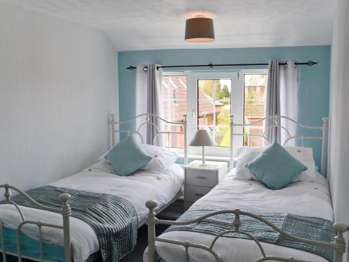 two beds in a room with blue walls and a window at Banovallum Cottage in Horncastle