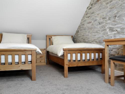 two twin beds in a room with a stone wall at Bwthyn Y Bugail in Felindre