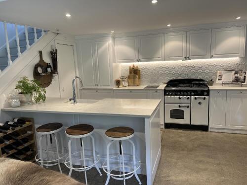 a kitchen with white cabinets and a island with bar stools at Dove Cottage in Auckland