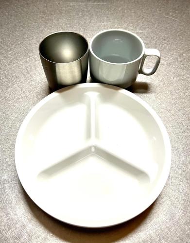 a white plate and a cup on a table at 一棟貸し宿OH!TOMARI-バレルサウナの有無選択できますo in Nanao