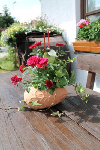 a flower pot with red flowers on a wooden table at Hotel Schäfflerhof in Bischofsmais