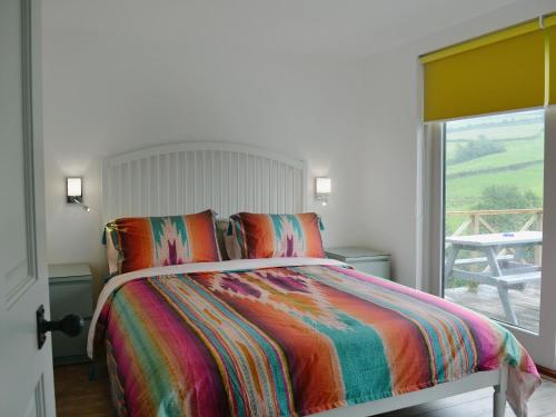 a bedroom with a bed with a colorful comforter and a window at The Shed With A View in Cadbury