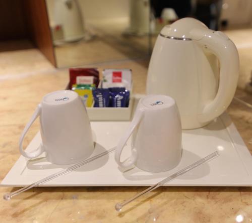 two white cups on a white plate with a tea kettle at Udman Hotel Haridwar in Haridwār