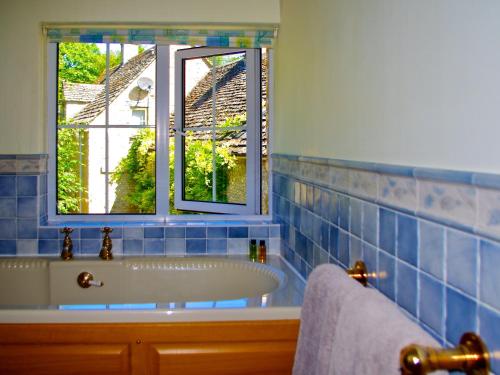 ein blau gefliestes Bad mit einer Badewanne und einem Fenster in der Unterkunft Ivy Cottage in Chedworth