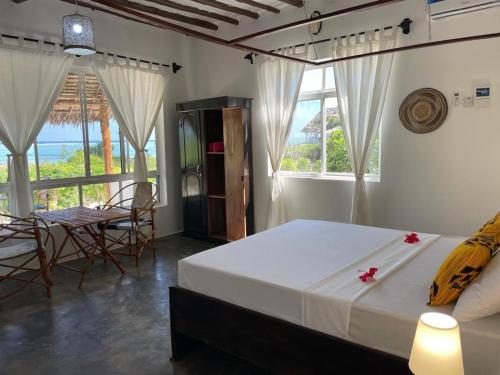 a bedroom with a bed and a table and windows at Matemwe Rock Villas in Matemwe