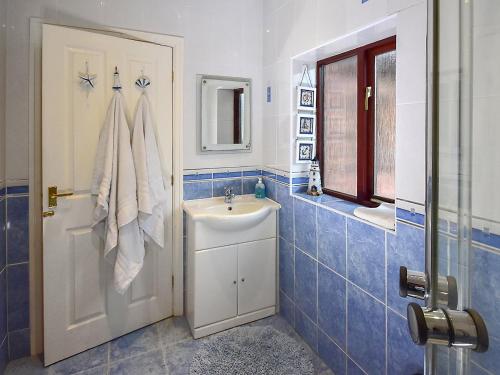 a blue tiled bathroom with a sink and a shower at South Lodge Cottage in Standish