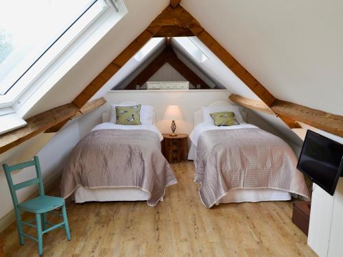 a attic bedroom with two beds and a chair at Whatley Lodge in Winsham