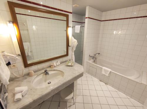 a bathroom with a sink and a tub and a mirror at Le Manoir Au Lac in Gérardmer