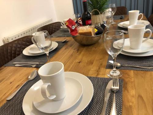 una mesa de madera con platos blancos y copas de vino en Montrose House - Spacious Comfy 3 Bedroom House, Free Wifi and Free Parking, en Swindon