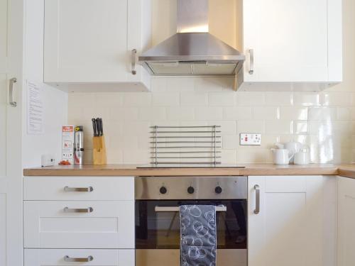 a kitchen with white cabinets and a stove top oven at Burdettes Cottage - 25349 in Findern