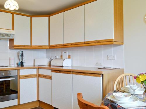 a kitchen with white cabinets and a dining table at Hannahs Cottage in Inverasdale