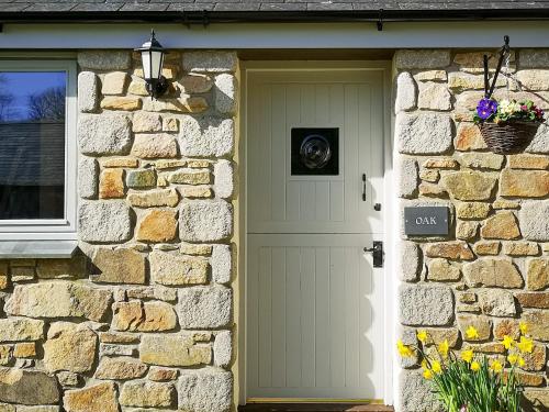 a white door of a stone house with flowers at Oak Barn in Porthtowan