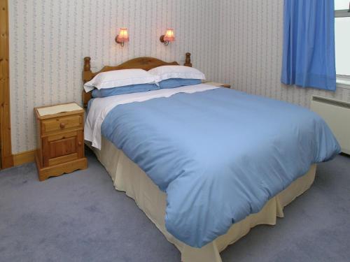 a bedroom with a large bed with a blue comforter at Middledrift Cottage in Brora