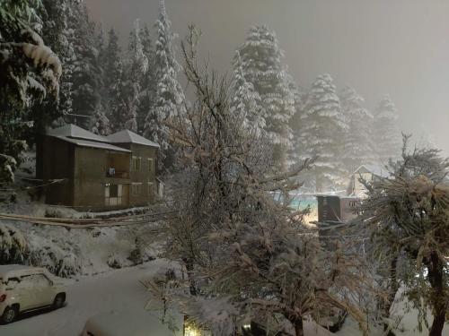a house covered in snow with trees and a car at Sparsh Resort, A Boutique Stay - Just 2kms uphill from Mall Road, near Old Manali in Manāli