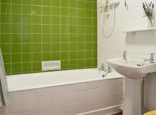 a green tiled bathroom with a tub and a sink at Cobden House in Lakenheath