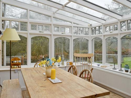 a conservatory with a wooden table in a room with windows at Jubilee Cottage in Enstone