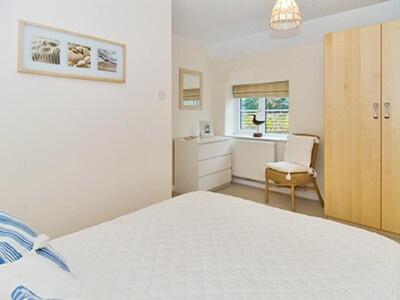 a white bedroom with a bed and a chair at Pebble Cottage in Holt