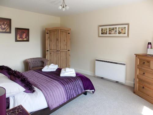 1 dormitorio con cama morada y armario de madera en Blaeberry Cottage - 28061, en Dinwoodie Mains