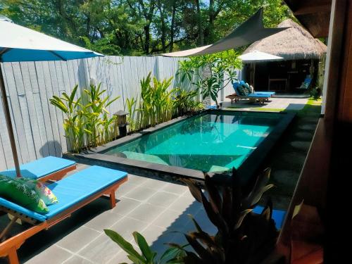 a swimming pool with two chairs and an umbrella at Little Lodge in Gili Trawangan