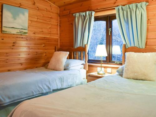 2 Betten in einem Zimmer mit Holzwänden und Fenstern in der Unterkunft Fern Lodge- Burnside Park in Keswick