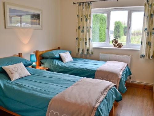 a bedroom with two beds and two windows at Peach Tree Cottage in Winterborne Steepleton