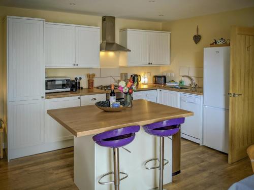 a kitchen with white cabinets and purple bar stools at Pleacairn Cottage in Dalton