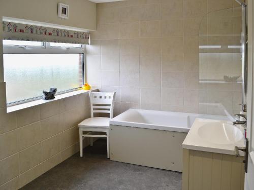 uma casa de banho com uma banheira, um lavatório e uma cadeira em Magnolia em Chickerell