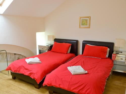 two beds with red sheets in a room at Oak Tree Barn - 27693 in Otterburn