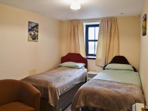 a room with two beds and a chair and a window at The Gatehouse in Aberffraw