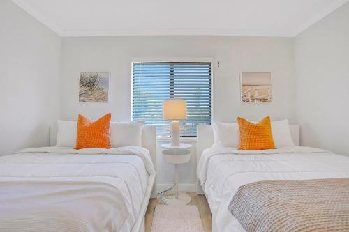 2 bedden in een witte kamer met oranje kussens bij Paralia Condo in Clearwater Beach